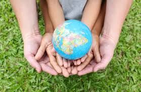 Quattro mani, due adulti e due bambini, che reggono una piccola sfera che rappresenta il globo terrestre, sopra un prato erboso.