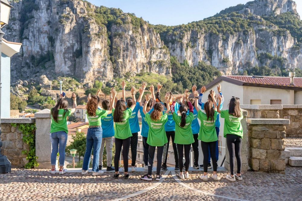 Gruppo di giovani con le magliette verdi e blu che alzano le mani, sullo sfondo una montagna rocciosa