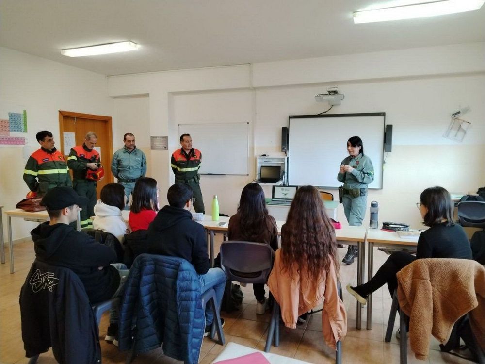 Un gruppo di persone in divisa da soccorritori parla con adolescenti seduti su sedie in un'aula scolastica