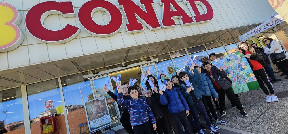 Gruppo di bambini in piedi fuori da un negozio Conad, con alcuni di loro che mostrano dei biglietti, mentre altri adulti osservano da destra.