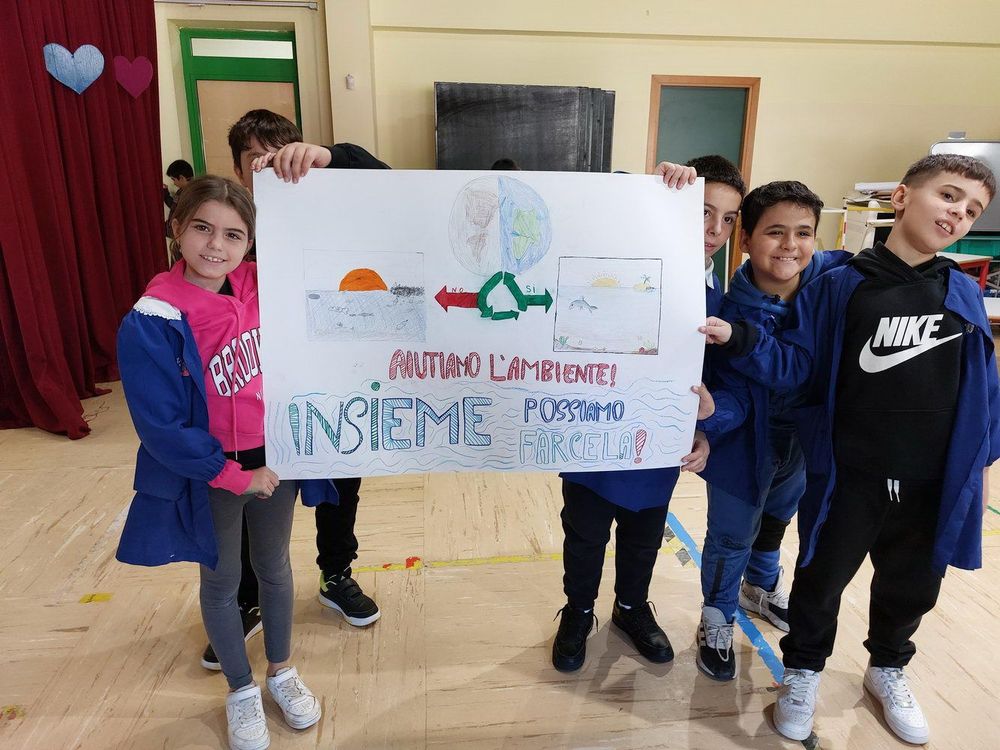 Gruppo di bambini in piedi che reggono un cartellone con disegni e messaggio su ambiente e sostenibilità