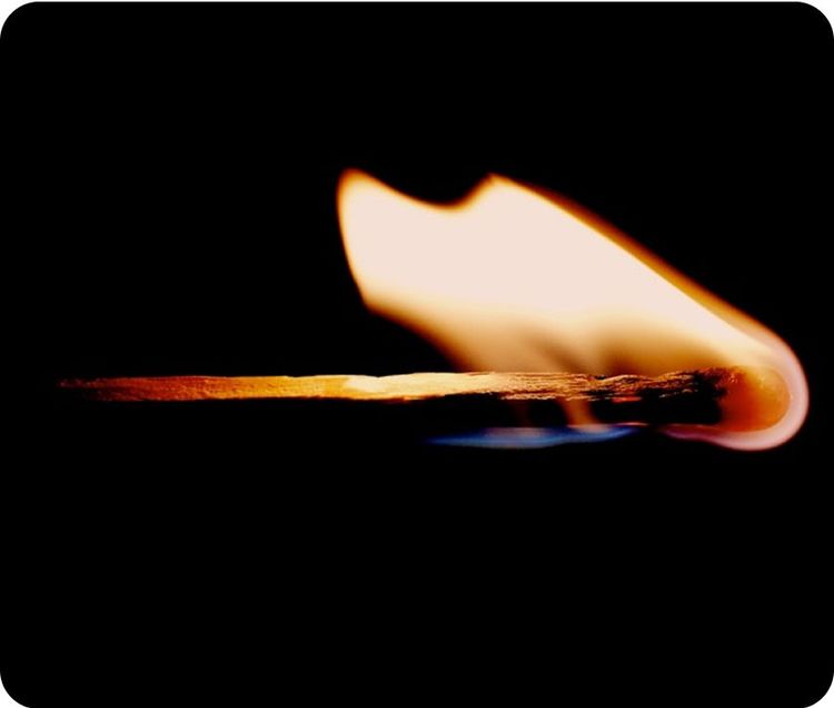 Un fiammifero acceso con fiamma arancione su sfondo nero