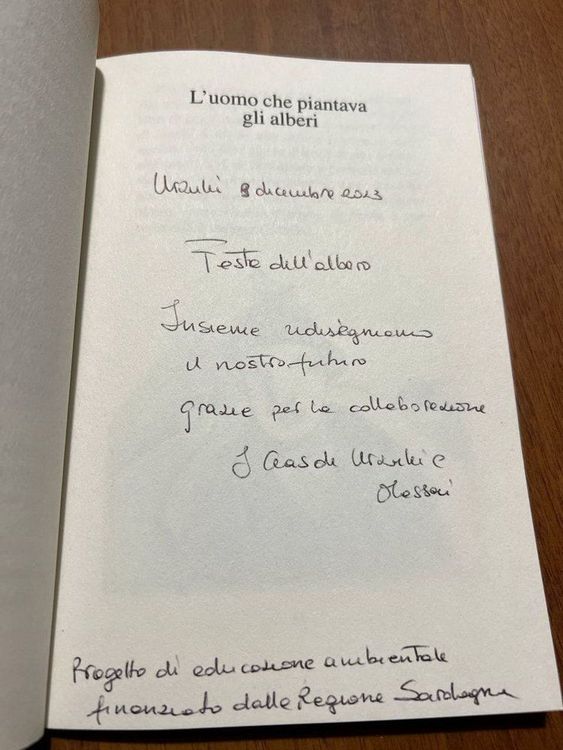 Una dedica scritta a mano su una pagina di un libro intitolato 'L'uomo che piantava gli alberi' su un tavolo in legno