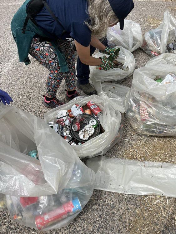 Una donna è china su un sacchetto di plastica pieno di rifiuti, mentre raccoglie oggetti da un mucchio di sacchetti di plastica pieni di spazzatura su