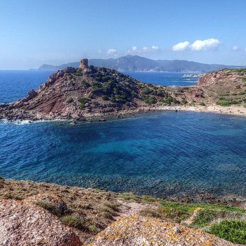 Veduta aerea di una baia con acque cristalline e una torre su un promontorio roccioso